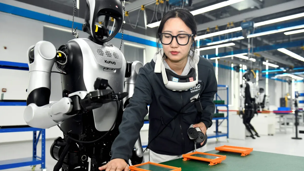 A trainer supervises a humanoid robot in an automotive manufacturing scenario in Shandong province, China. (Getty Images)