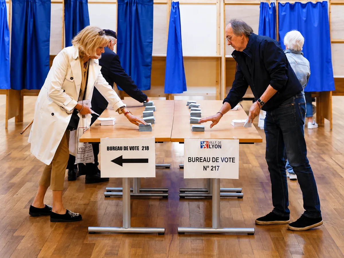 Voters take ballots from stacks displayed on tables in the second round of the 2022 French presidential election at a polling station in Lyon, France (Stephane Mahe/Reuters)